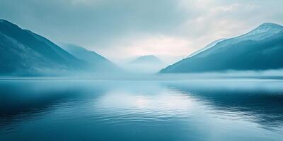 Serene blue landscape featuring a calm lake reflecting surrounding misty mountains, creating a peaceful and scenic view. photo
