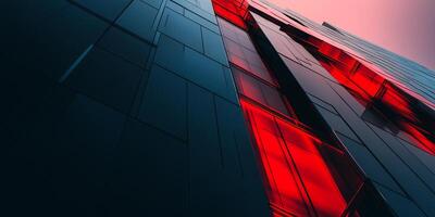 Dramatic low angle view of a modern building with blue and red glass panels reaching towards a soft pink and orange sky at dusk. photo