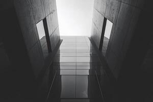 Monochromatic photo from ground level of a tall, modern building with glass and concrete, reaching for the sky above in an architectural shot.
