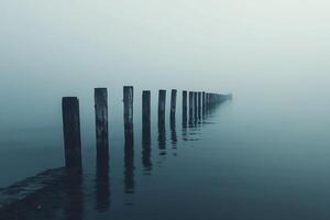 Eerie row of weathered posts in foggy water, creates a melancholic and captivating seascape with muted, misty tones and mysterious atmosphere. photo
