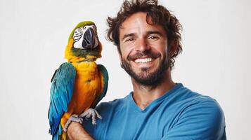 A happy man smiles with a colorful macaw parrot perched on his arm in a studio setting. The parrot has blue, yellow and green feathers. photo