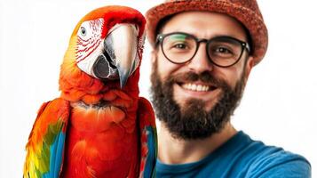 A cheerful man with a beard and glasses smiles beside a colorful macaw parrot in front of a white background. Friendship concept. photo