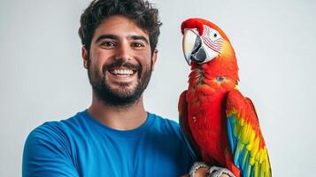 Portrait of a smiling man with a vibrant scarlet macaw parrot perched on his arm, showcasing their unique bond in front of a neutral backdrop. photo