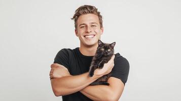 A happy smiling man in a black shirt holding a fluffy black kitten in his arms with white studio backdrop, perfect for a heartwarming pet adoption post. photo