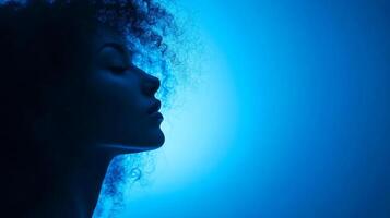 Profile of a woman with curly hair, bathed in a monochromatic blue light with her face illuminated on a dark background. photo