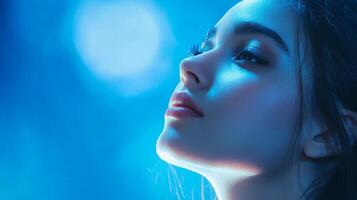 A serene close-up captures the graceful curve of a woman's face against a soothing blue backdrop. The image evokes tranquility and introspection. photo