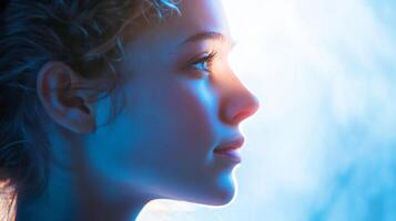 Profile of a woman illuminated by light. She is facing to the right in this glowing image, with blues, pinks and whites on her skin. photo