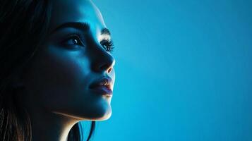 Glamorous woman illuminated in vibrant blue light, looking up with a serene expression. A portrait embodying beauty and introspection. photo