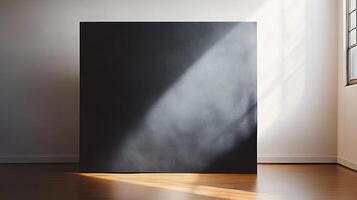 A square dark board casting a long shadow against a white wall, sitting on a glossy wood floor, next to a window's light. photo