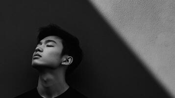 Portrait of a person with eyes closed, leaning against a wall with dramatic lighting creating a contemplative, serene atmosphere. photo