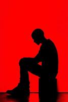 Silhouette of a person sitting against a vibrant red backdrop photo