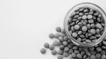 Gray tablets spilled from a glass jar on a plain surface photo