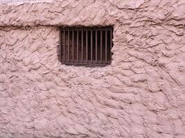 A square ventilation grille with a pattern of metal on a pink plastered wall photo