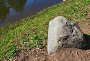 A huge boulder lies on the green grass near the river path in the park photo
