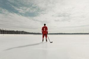 An ice hockey player wearing a red jersey and helmet, skating on the ice of a frozen lake, showcasing athleticism and winter sports energy photo