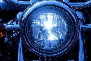 Close-up shot of the headlight on a vintage motorcycle with a cool blue tone, showcasing its classic design and reflective surface photo