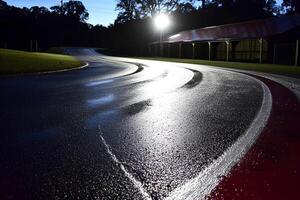 Nighttime view of a racing track with white markings on the asphalt road, illuminated by lights, creating an exciting and dynamic atmosphere photo