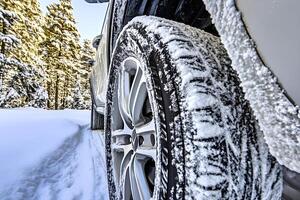 Close-up of winter tires covered with snow, positioned on a snowy road surrounded by a peaceful forest in winter photo