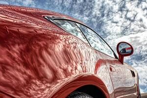 Close-up shot of a vibrant red car parked under a clear blue sky with fluffy clouds, highlighting its sleek design and the peaceful atmosphere photo