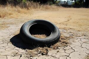 Old tire lying on dry ground in a field, representing drought and environmental concerns photo