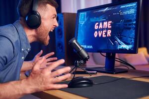 A man is screaming at a computer screen with the words game over photo