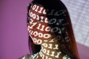 A woman with her face projected onto a wall with binary code photo