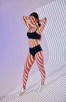 A woman in a black bikini top and shorts standing in front of a light photo