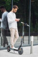 A man is standing on a scooter looking at his phone photo