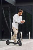 A man is standing on a scooter and looking at his phone photo