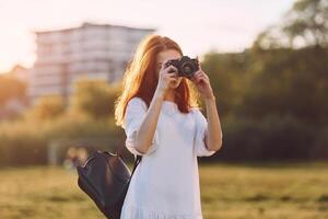 Holding a camera. Young girl is on the field at sunny daytime having nice weekend photo