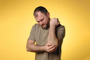 Man suffers from elbow pain due to negative impact of long-term computer work, bad posture, uncomfortable workplace. Concept of comfortable work space to avoid joint pain and health problems photo