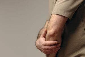 Man suffers from elbow pain due to negative impact of long-term computer work, bad posture, uncomfortable workplace. Concept of comfortable work space to avoid joint pain and health problems photo