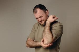 Man suffers from elbow pain due to negative impact of long-term computer work, bad posture, uncomfortable workplace. Concept of comfortable work space to avoid joint pain and health problems photo