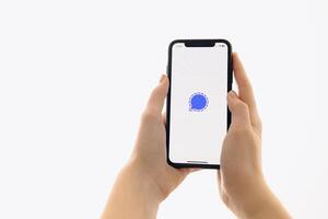 Zaporizhia, Ukraine - January 10, 2025. A woman holds an iPhone with the Signal app logo on the screen while using a mobile app for business at home. white background photo