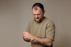 A man holds his wrist in pain. The hand tightly clasps the affected area, emphasizing the soreness and need for support. Pain and suffering in the wrist interfere with professional activities. photo