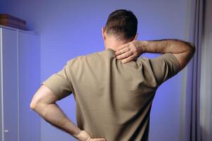 man suffers from back pain due to negative impact of long work at computer, bad posture, uncomfortable work place. Concept of comfortable work space to avoid joint pain and health problems photo