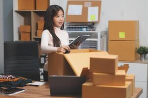 A woman is holding a tablet while sitting at a desk with boxes photo