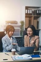 Two women in business attire sitting at a table with a laptop photo