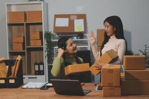 Two women are talking while sitting at a desk with boxes photo