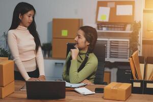 Two women sitting at a desk with boxes and papers photo