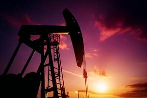 Silhouetted oil pump jack under a vibrant sunset with colorful clouds in the background photo