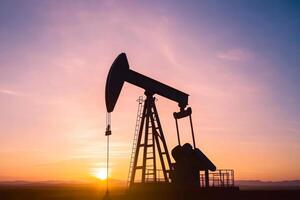 Oil pump jack operating at sunset in an open field with colorful sky and silhouettes photo