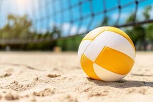Bright yellow and white volleyball resting on sandy court under clear blue sky during sunny day in a recreational area photo