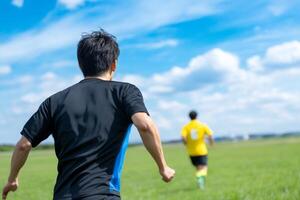 Two young men running on a green field under a bright blue sky in a friendly competition photo