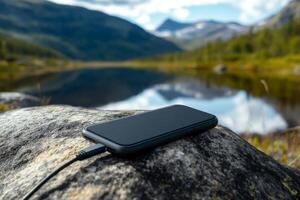 Smartphone charging by a tranquil lake with mountains in the background during a sunny day photo