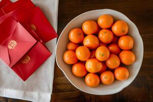 Bowl of vibrant tangerines with red envelopes for Chinese New Year, symbolizing prosperity and good luck photo