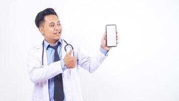 Asian Male Doctor Showing Blank Screen Mobile Phone Mock Up and Raising Thumb Up on White Background photo
