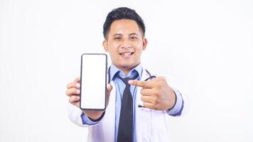Portrait of Handsome Asian Male Doctor Pointing at Mobile Phone with Blank Screen Mock Up on White Background photo