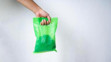 Hand Carrying Green Plastic Bag with Copy Space on White Background photo