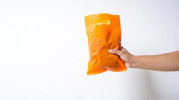 Hand Holding Orange Plastic Bag with Copy Space on White Background photo